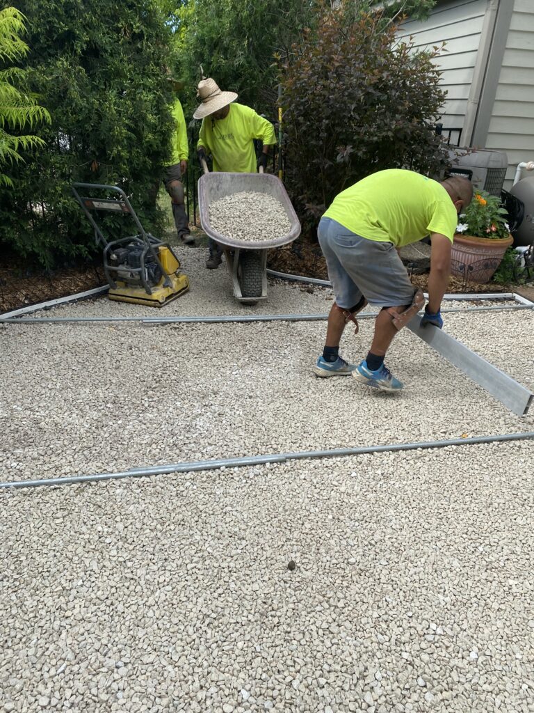 Pictured you'll see a man with a wheel barrel loading clear stone for another worker to screed the pet turf base designed for drainage to be smooth and ready for pet turf installation in Wisconsin.